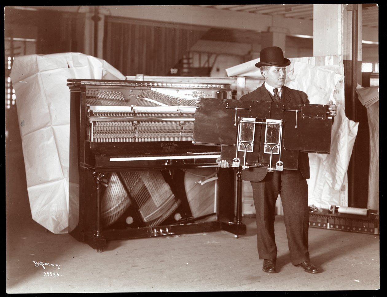 Ricca und Son Piano Co. -yhtiön piano, jonka vieressä oleva mies pitelee osaa pianon teoksista, 1907 (hopeagelatiinivedos). tekijältä Byron Company