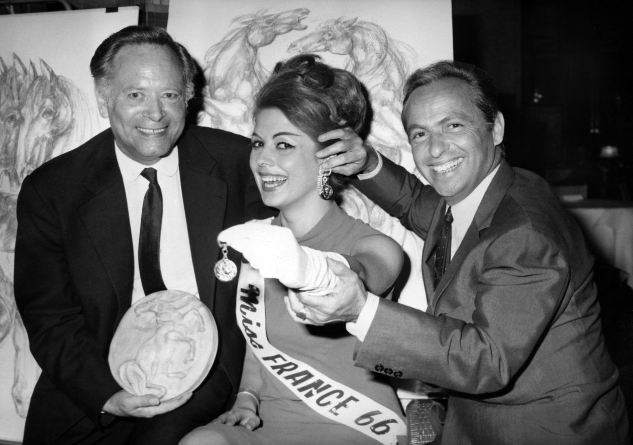 Rene Bollinger (vasemmalla) ja Guy Lux Entourent Monique Boucher "Miss France" kenelle he vain ojensivat avaimenperän "Talisman Du Turfiste" Bollingers-kankaan avajaisissa 12. heinäkuuta 1966 tekijältä Unknown