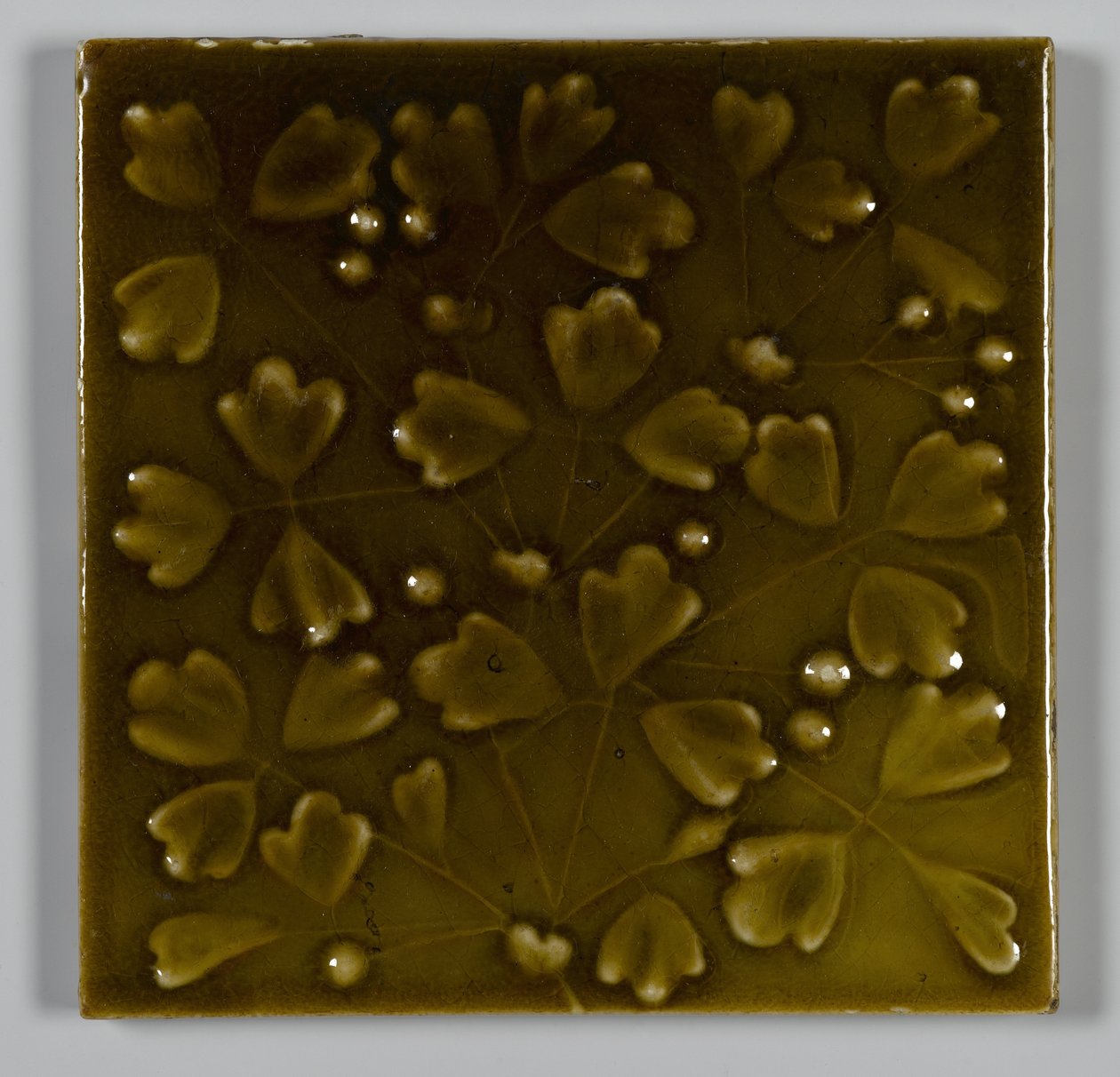 Laatta on suunniteltu ja valmistettu J. & J.G. Low Art Tile Works, Chelsea, Massachusetts, n. 1881 (lasitetut keramiikka) tekijältä American School