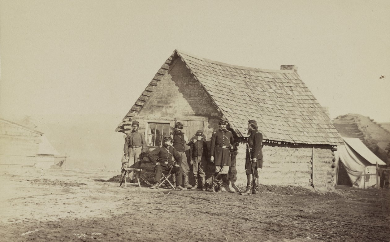 Ryhmä sotilaita ja kaksi nuorta miestä, joista toinen on afroamerikkalainen, seisoo hirsimökin ulkopuolella, 1861-65 tekijältä American Photographer