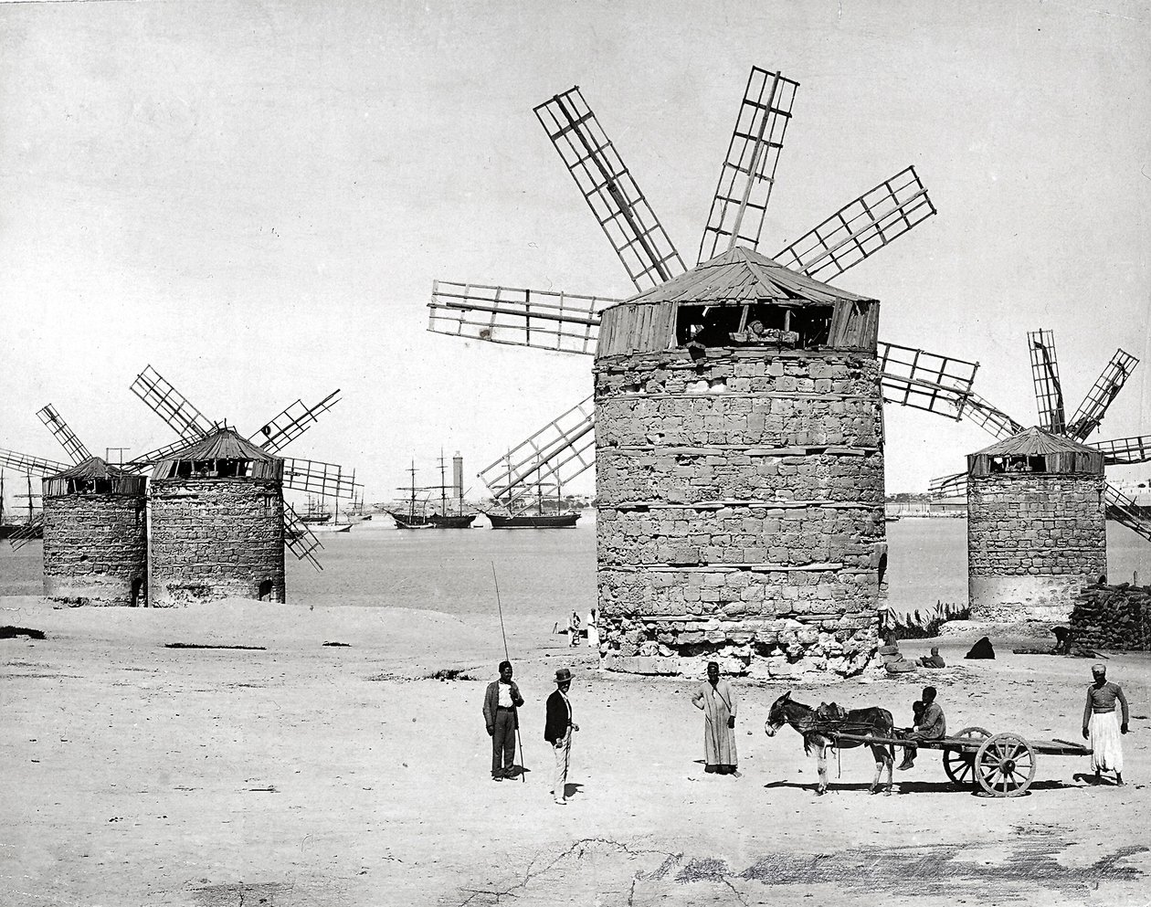 Tuulimyllyjä Välimerellä Aleksandriassa, Egyptissä. Edessä poseeraavat egyptiläiset pienen kärryn kanssa. tekijältä Brothers Zangaki