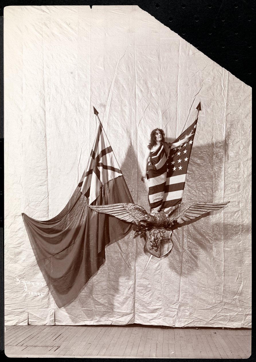 Elävä kuva: Amerikan lippuun verhoutunut malli seisoo kaljukotkan veistoksen päällä, 1900 tai 1901 (hopeagelatiinivedos). tekijältä Byron Company
