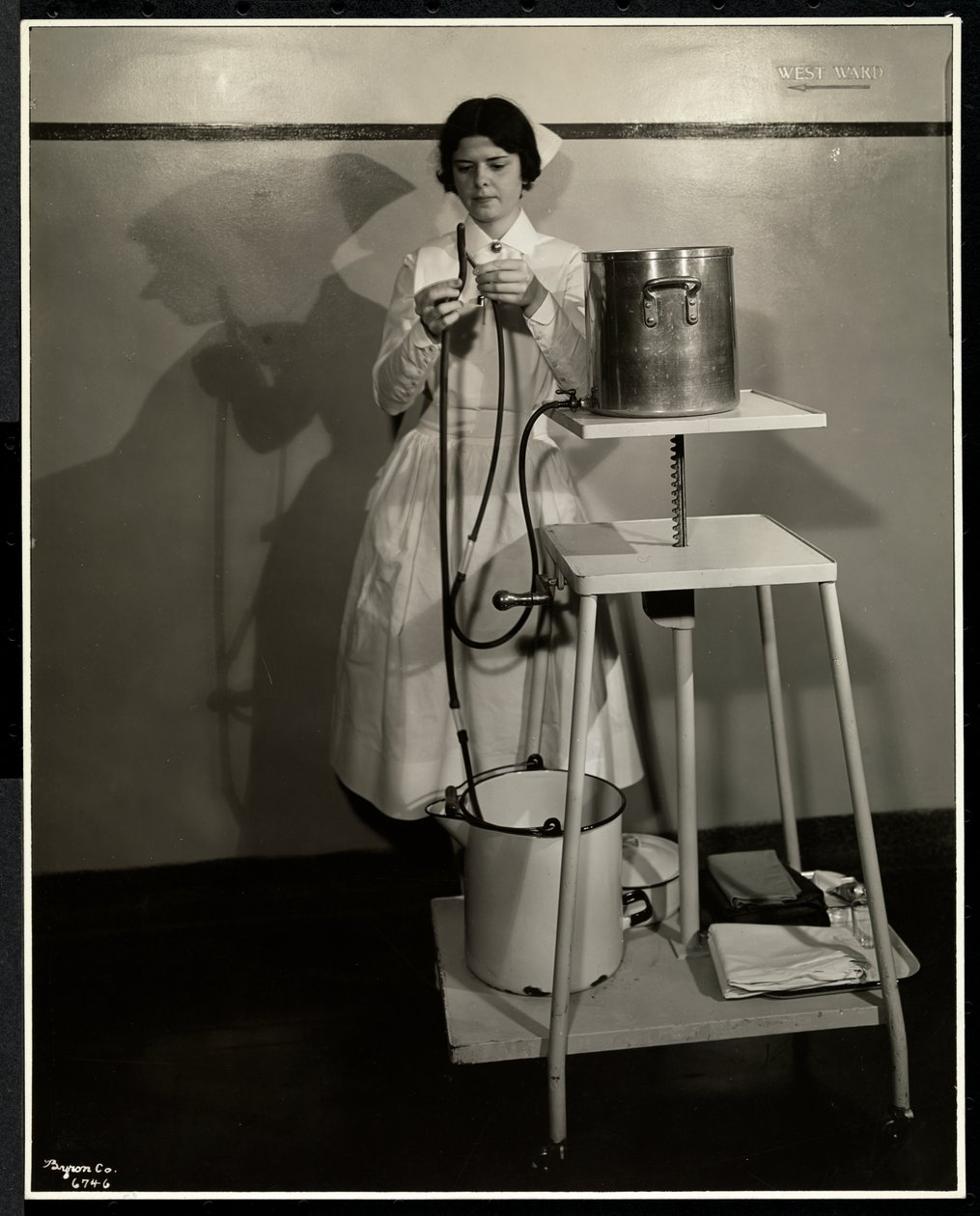 Sairaanhoitaja esittelee erikoislaitetta, jossa on putkia ja syöttö- ja jäteastioita Sloan Maternity Hospitalissa, Broadwayssa ja 168th Streetissä, New Yorkissa, 1932 (hopeagelatiiniprintti) tekijältä Byron Company