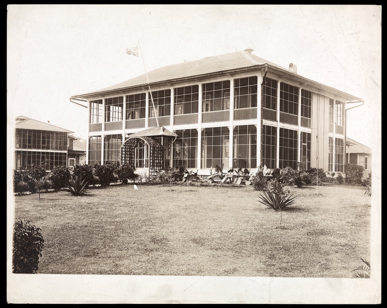 Kaksikerroksinen kuistien ympäröimä talo, jossa liehuu Yhdysvaltain lippu; Panamassa kanavan rakentamisen aikana, 1912 (hopeagelatiiniprintti) tekijältä Byron Company
