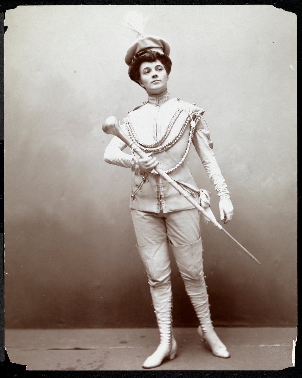 Nainen mallinnuspukua, kädessään sauva, n. 1898 (hopeagelatiiniprintti) tekijältä Byron Company