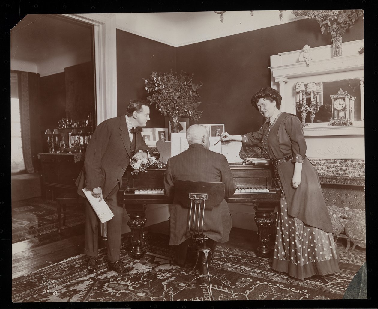Clara De Regand osoittaa partituuria miehen soittaessa pianoa, 1910 (hopeagelatiiniprintti) tekijältä Byron Company