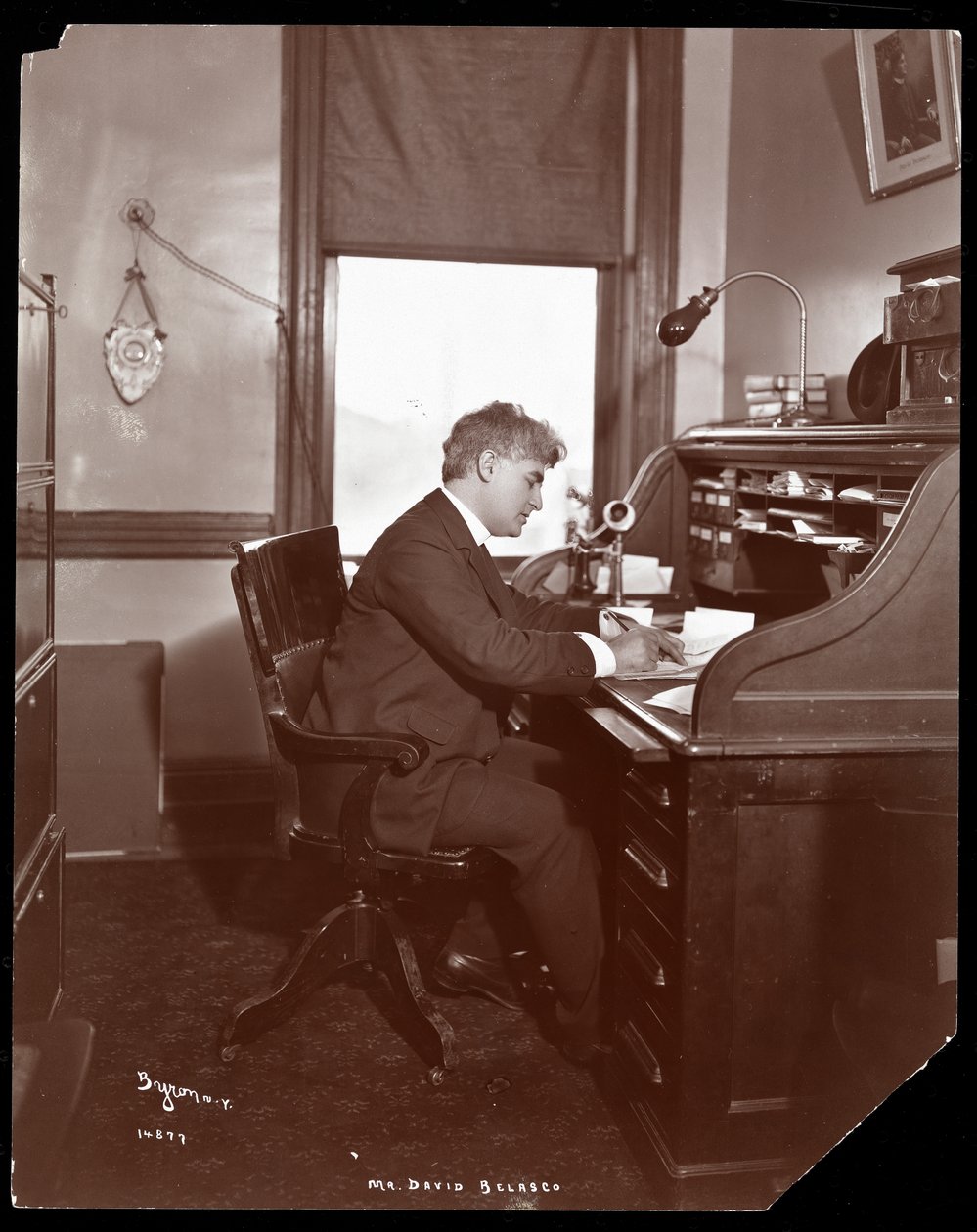 David Belasco kirjoittaa kirjoituspöydän ääressä teatterinsa toimistossa, 1902 (hopeagelatiinipaino). tekijältä Byron Company