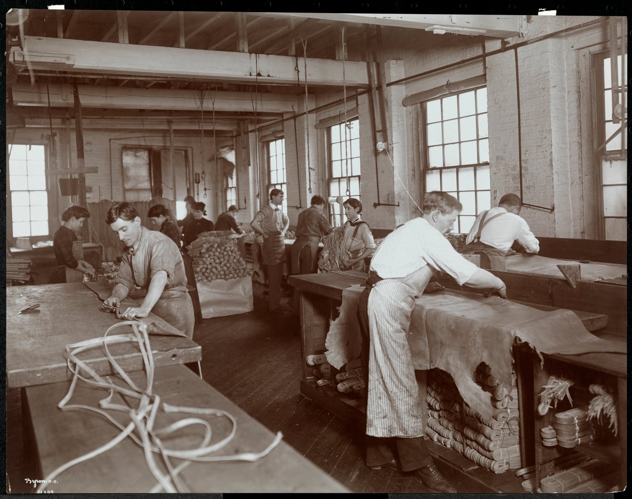 Sisäkuva miehistä ja naisista, jotka työskentelevät nahkaa New York Leather Belting Co.:ssa, New York, 1906 (hopeagelatiiniprintti) tekijältä Byron Company