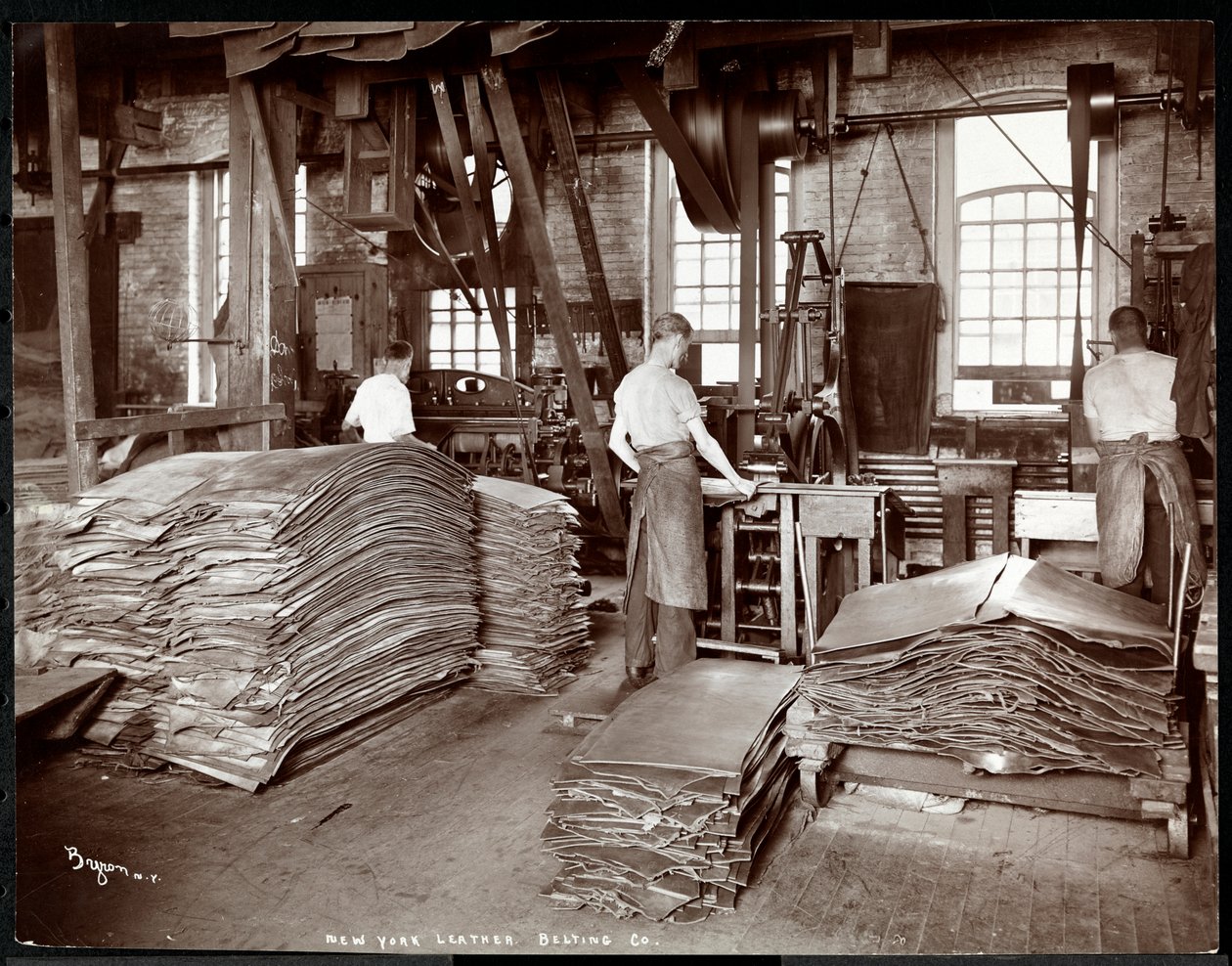 Sisäkuva kolmesta miehestä, jotka työskentelevät nahan ja raskaiden laitteiden kanssa New York Leather Belting Co.:ssa, New York, 1905 (hopeagelatiiniprintti) tekijältä Byron Company
