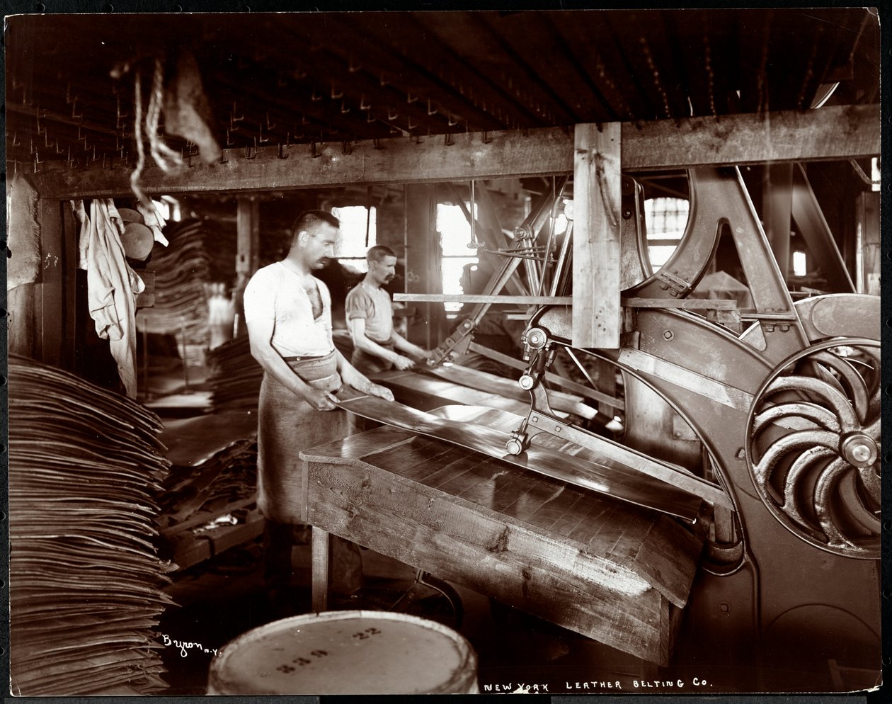 Sisäkuva kahdesta miehestä, jotka työskentelevät nahan ja raskaiden laitteiden kanssa New York Leather Belting Co.:ssa, New Yorkissa, 1905 (hopeagelatiiniprintti) tekijältä Byron Company