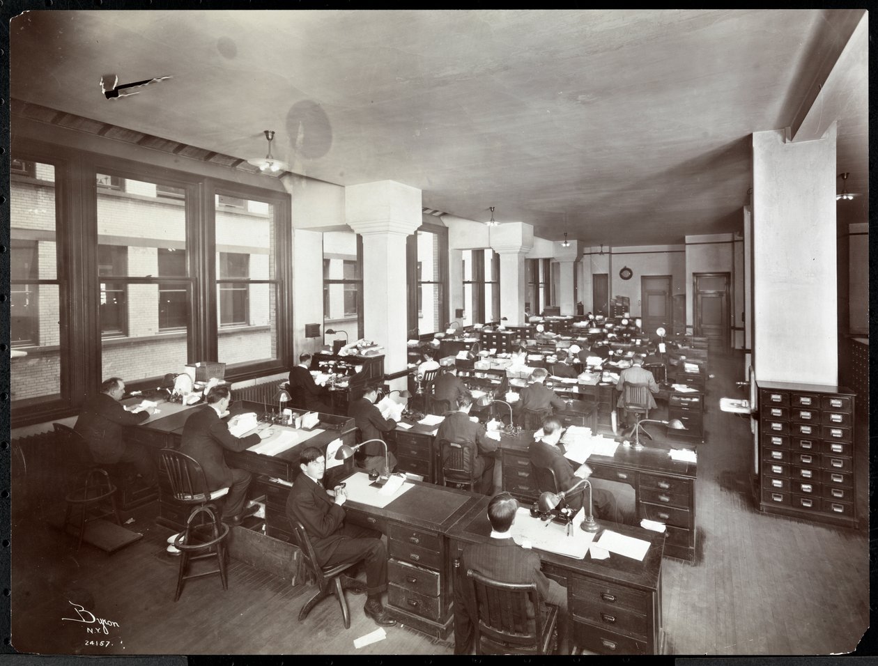 Miehet ja yksi nainen työskentelevät työpöydän ääressä Metropolitan Life Insurance Co:n toimistossa osoitteessa 23rd Street ja Madison Avenue, New York, 1907 (hopeagelatiiniprintti) tekijältä Byron Company