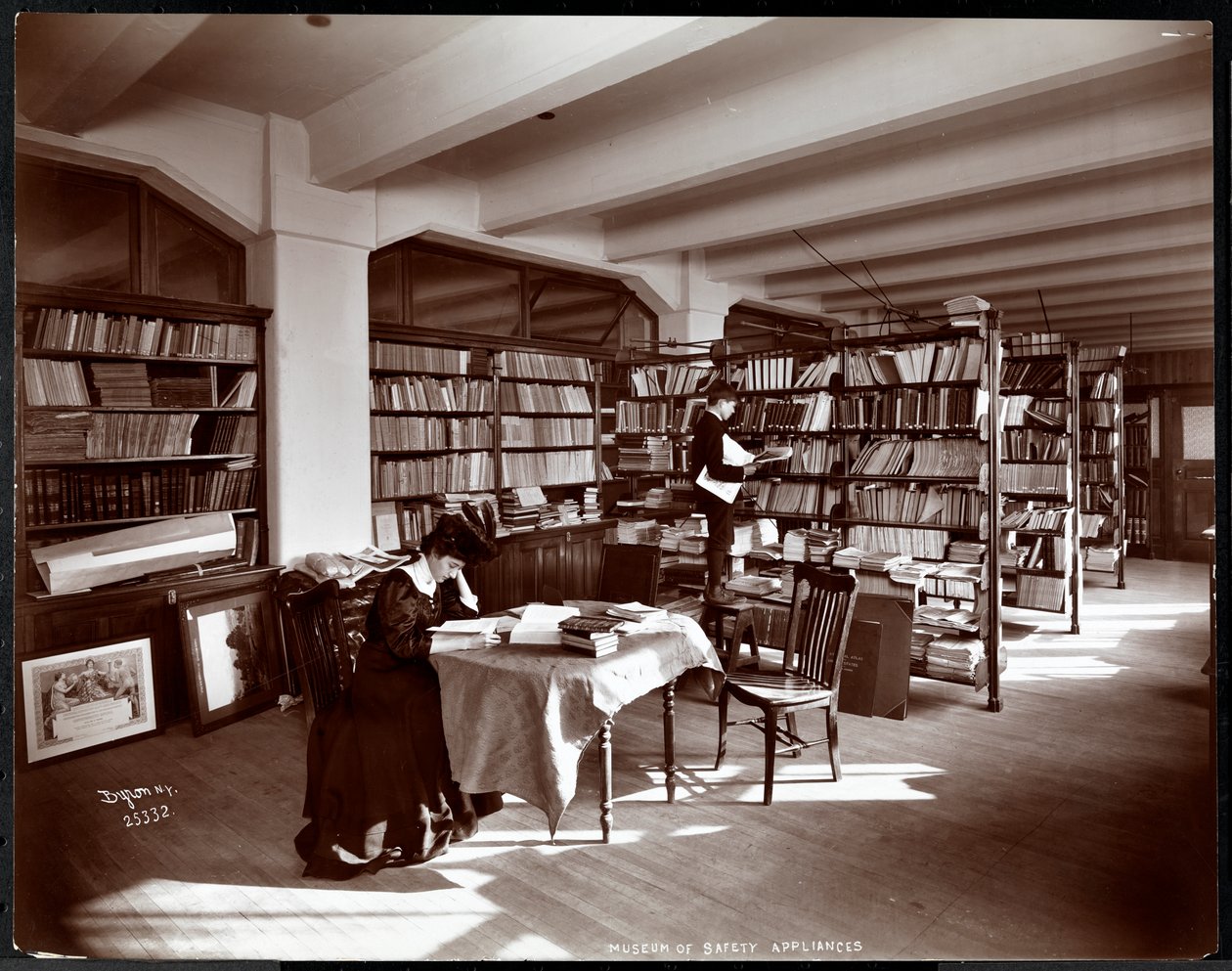 Nainen ja nuori mies American Institute of Social Servicen turvallisuuslaitteiden museon kirjastossa, New York, 1907 (hopeagelatiiniprintti) tekijältä Byron Company