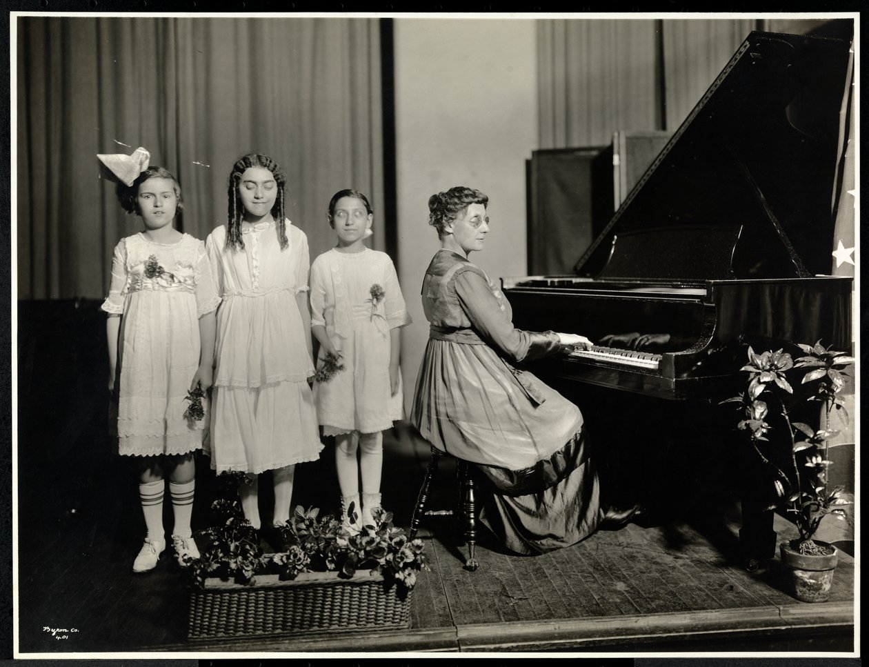 Nainen soittaa pianoa, kun kolme tyttöä laulaa New York Association for the Blindissa, 111 East 59th Street, New York, n. 1917 (hopeagelatiiniprintti) tekijältä Byron Company