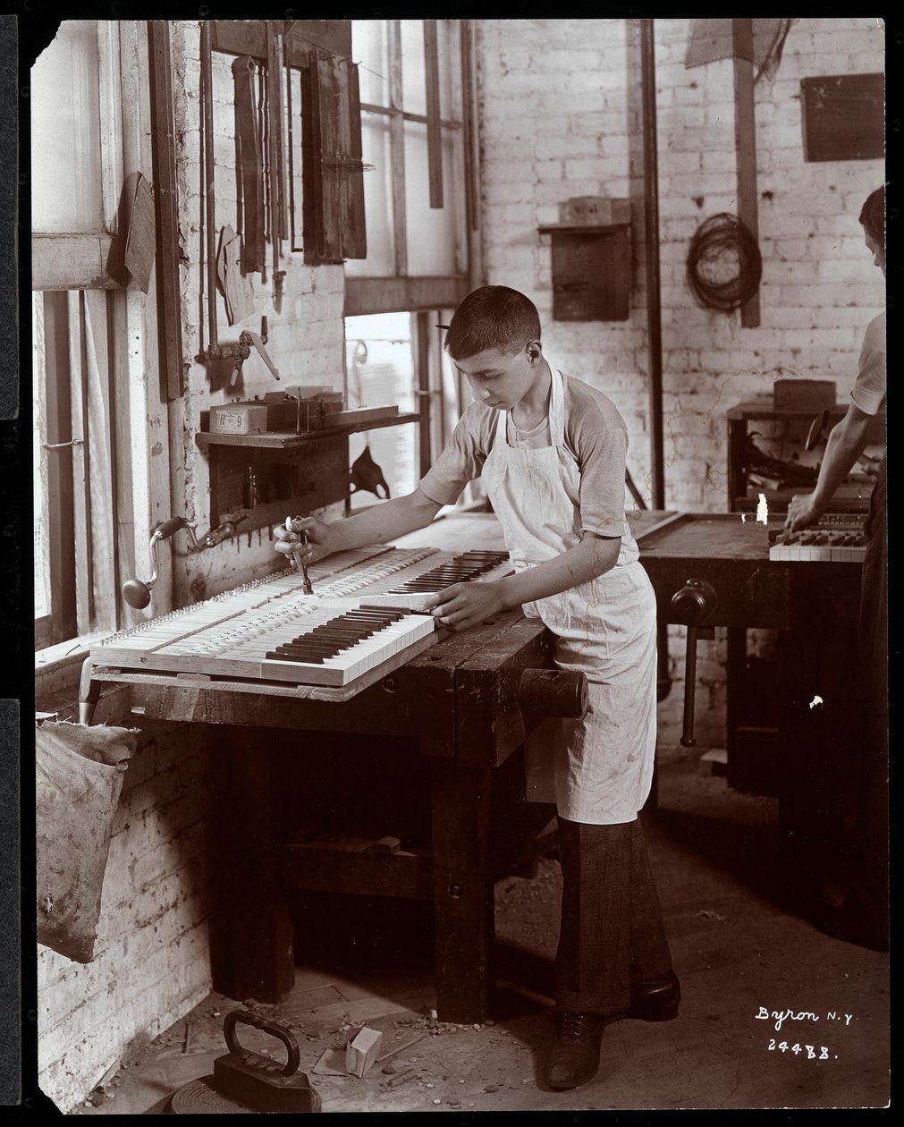 Nuori mies työskentelee Harrington Piano Co:n tehtaalla, 1907 (hopeagelatiinipaino) tekijältä Byron Company