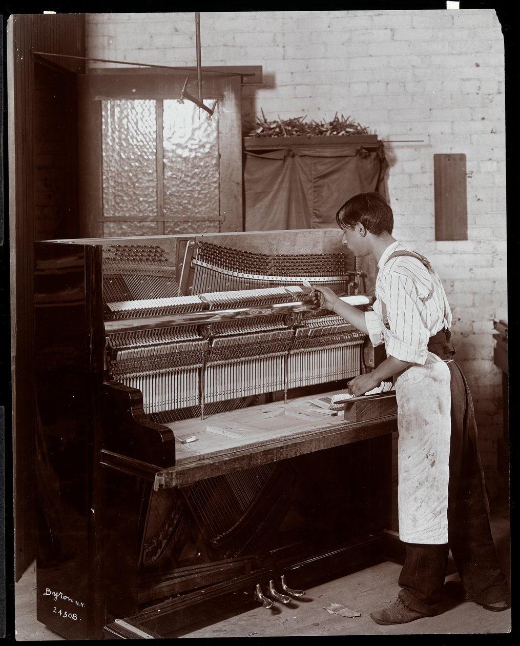 Mies työskentelee Hardman, Peck und Co:n pianotehtaalla, New York, 1907 (hopeagelatiiniprintti) tekijältä Byron Company