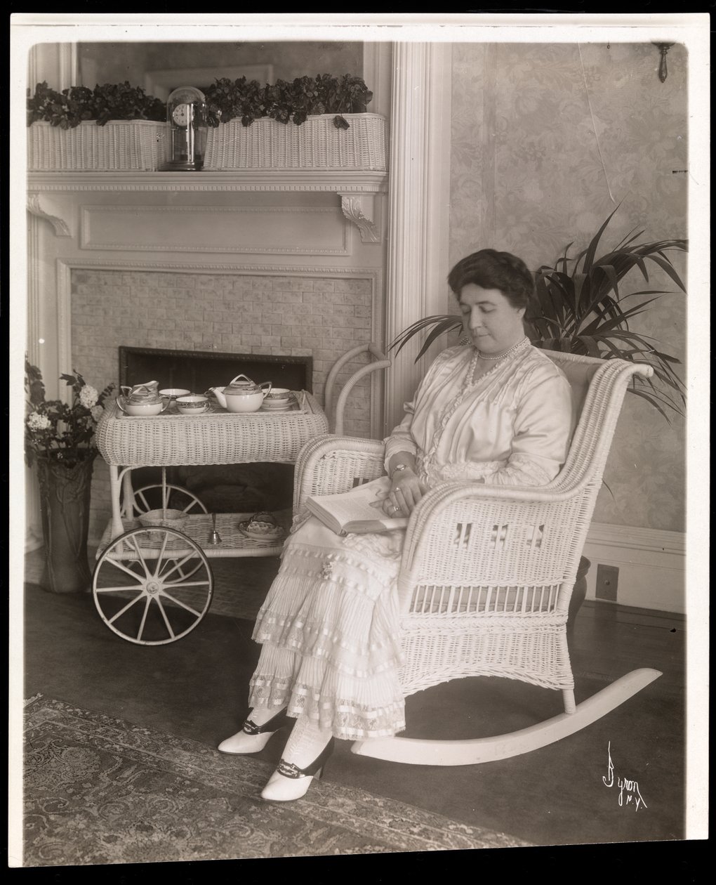 Rouva Howard istuu kirjan kanssa keinutuolissa kotonaan osoitteessa 200, 5th Avenue, New York, 1915-1916 (hopeagelatiiniprintti) tekijältä Byron Company