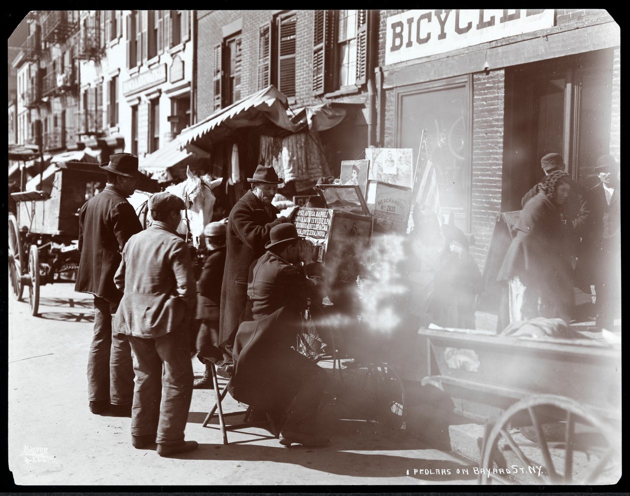 Näkymä katukauppiaista, mukaan lukien yksi, joka näyttää valokuvallisia näkymiä eksoottisista paikoista näköalalaatikossa Bayard Streetillä, New Yorkissa, 1898 (hopeagelatiiniprintti) tekijältä Byron Company