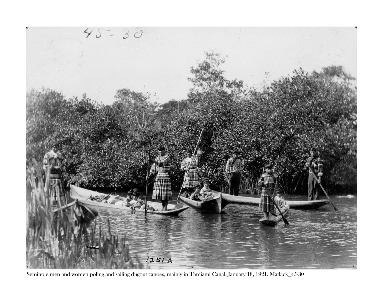 Seminole-miehet ja -naiset sauvoivat ja purjehtivat korsuja kanootteja Tamamin kanavalla, 18. tammikuuta 1921 tekijältä Claude C. Matlack