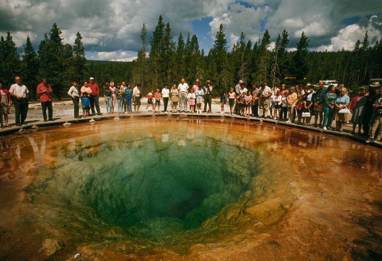 Puiston kävijät kokoontuvat sinivihreän, kukanmuotoisen lämpöaltaan ympärille. Yellowstone Nati... tekijältä Dean Conger