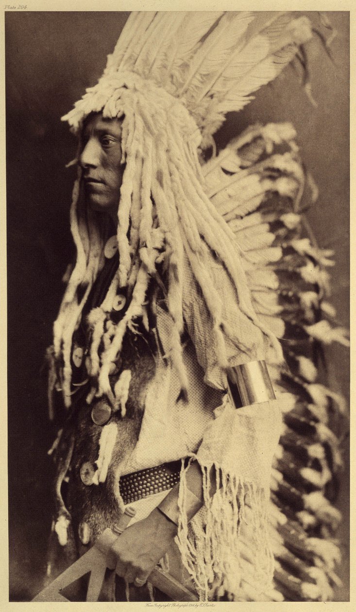 Vanha henkilö, Piegan. Nuoret miehet eivät kaipaa julkisia juhlia pukeutuakseen soturi-isänsä vaatteisiin. Kuva otettu Edward S. Curtisin (1868-1952) Pohjois-Amerikan intiaaneja käsittelevän tietosanakirjan osasta 6, jossa on etuosa tekijältä Edward Sheriff Curtis