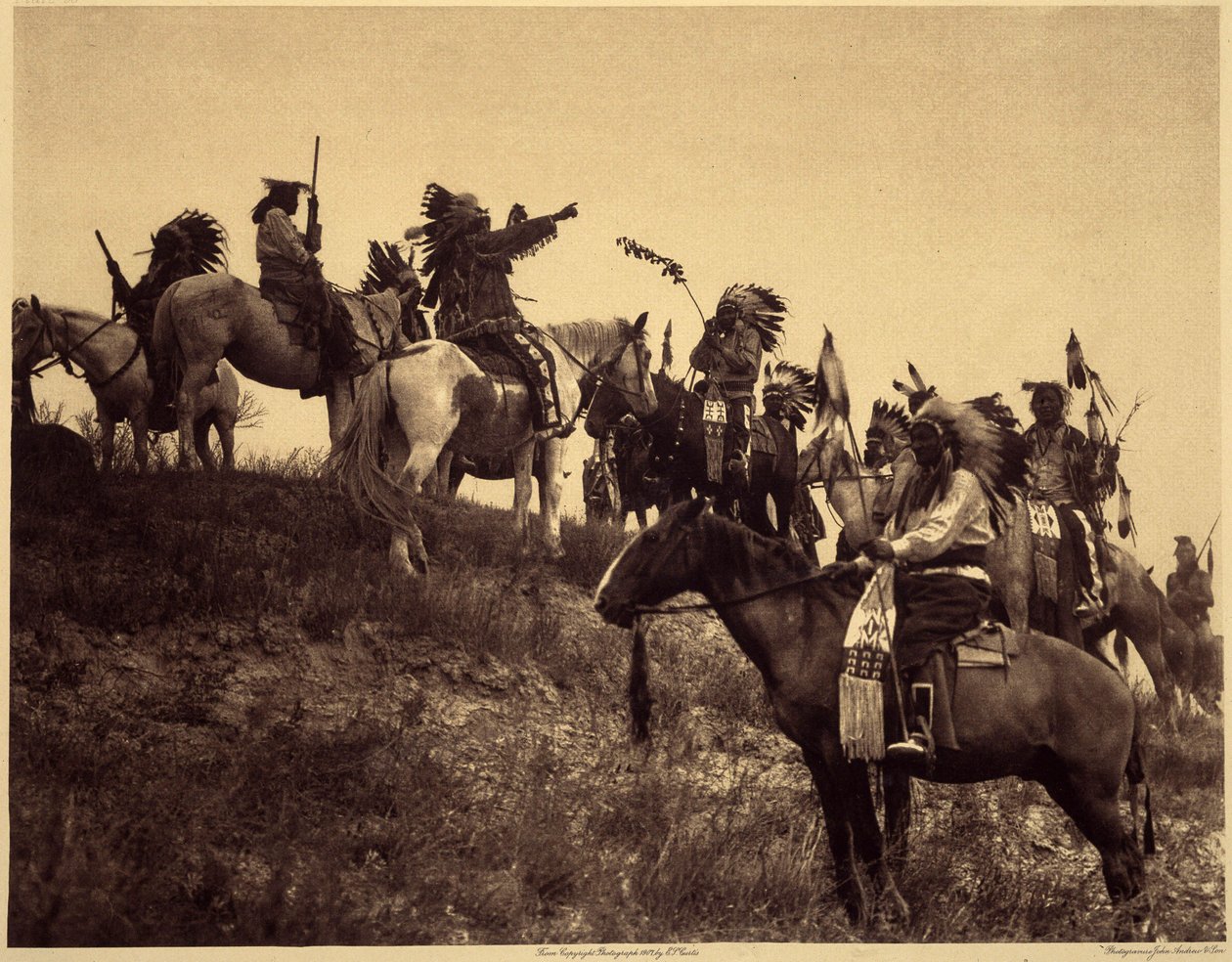 Raidan suunnittelu. Intiaanit kokoontuvat vaikuttavissa tyypillisissä puvuissaan äärimmäisen viehättäväksi ryhmäksi. Tämä on joukko Sioux Ogalalasta (Oglala), kukkulalla, josta on näkymät Wounded Knee Valleyyn Pine Ridge Reserve -alueella Etelä-Dakotassa.  tekijältä Edward Sheriff Curtis