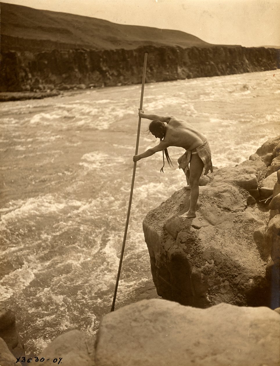 Tlakluit-intiaani, seisoo kalliolla, kalastaa verkolla, n.1910 (s/w valokuva). tekijältä Edward Sheriff Curtis