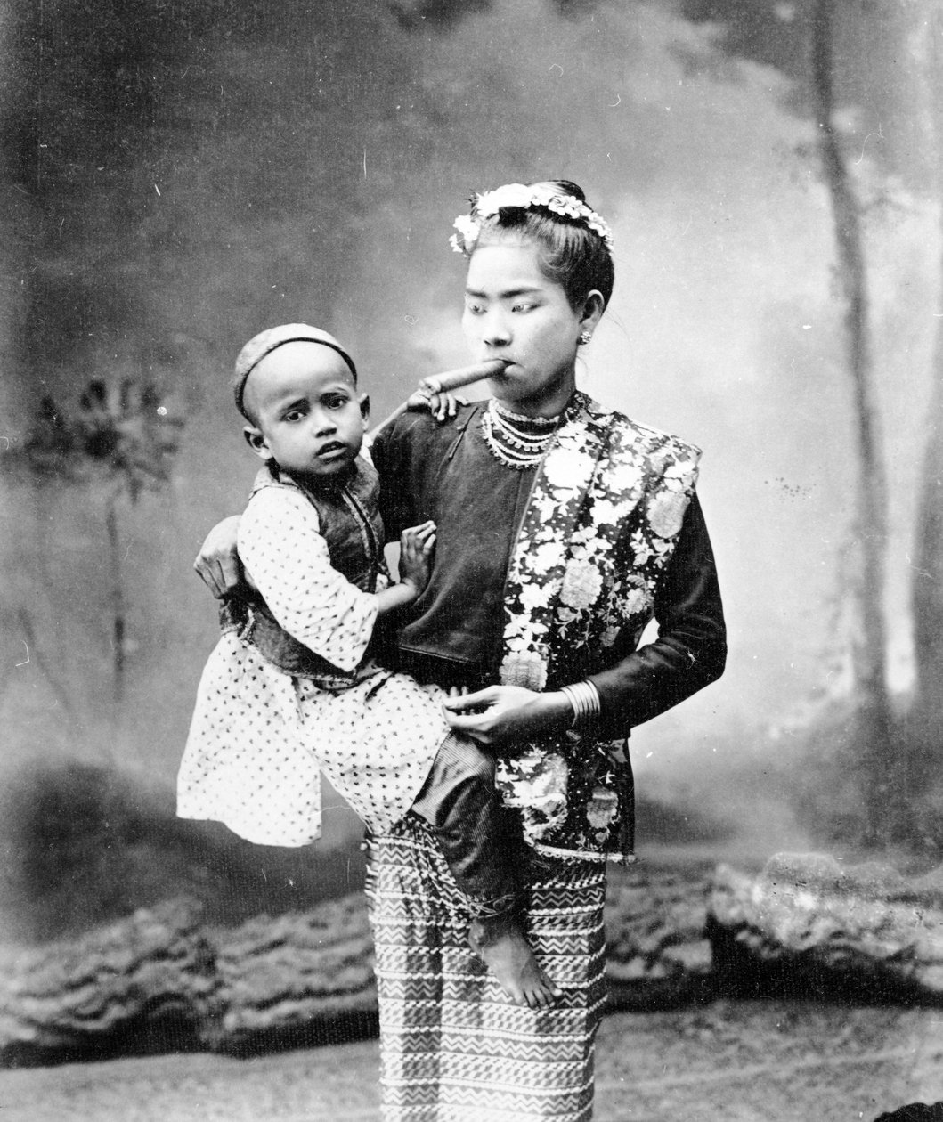 Burmalainen nainen lapsen kanssa ja polttaa Cherootia, n. 1870-1890 tekijältä English Photographer