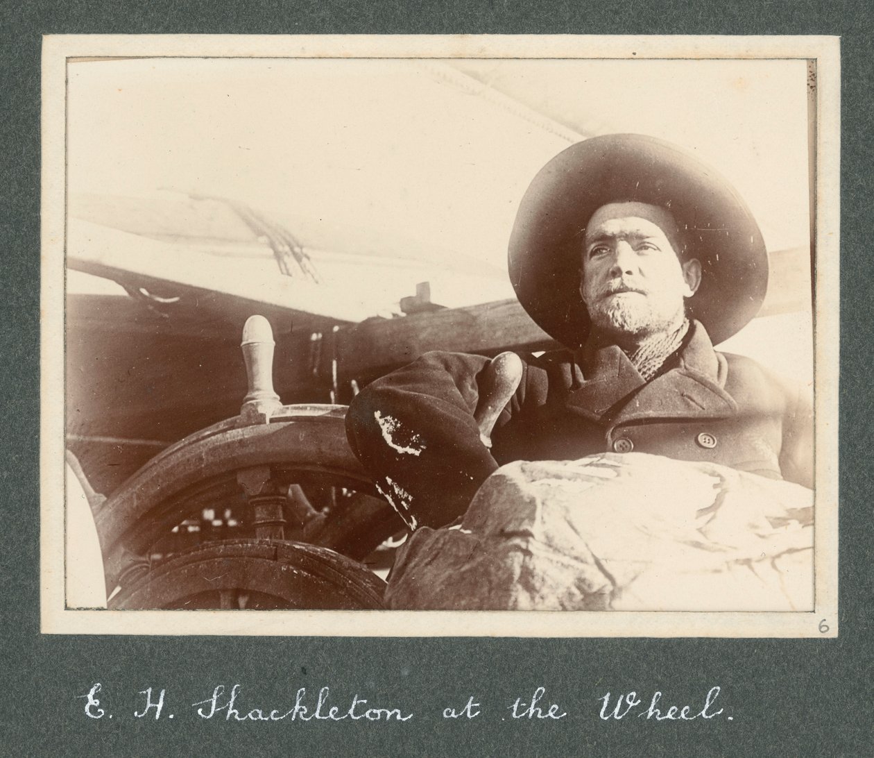 E H Shackleton seisoo Discovery-aluksen ratissa (1901) Sir Ernest Henry Shackletonin albumista National Antarctic Expedition (1901-1903). tekijältä Ernest Henry Shackleton