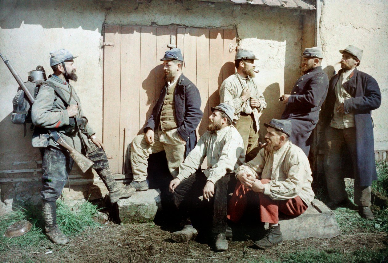 Seitsemän ranskalaista sotilasta rakennuksen edessä, yksi kantaa aseita ja varusteita, Ranska, n. 1914-18 (autokromi) tekijältä French Photographer