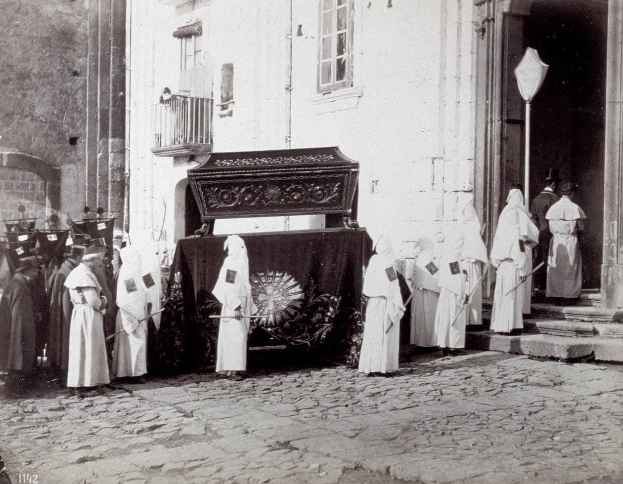 San Francescon seurakunnan hautajaiskulkue Napolissa. Etualalla, kirkon edessä, lukuisat "veljesveljet" valkoisissa tunioissa ja hupuissa seuraavat katafalkkia, joka on koristeltu brodeeratulla kankaalla, jonka päälle arkku asetetaan. tekijältä Giorgio Sommer