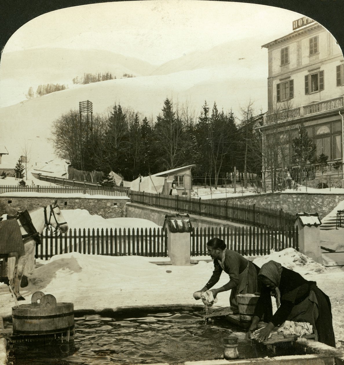 Naiset pesemässä vaatteita julkisella suihkulähteellä keskitalvella, Zuoz, Sveitsi tekijältä H. C. White