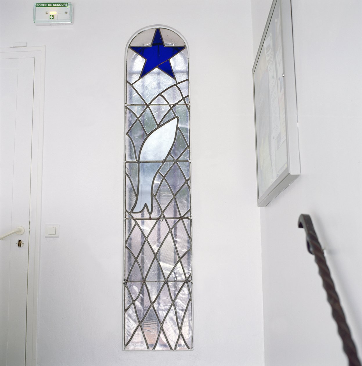 Rukousnauhan kappeliin johtavilta portailta lasimaalaus, joka esittää verkkoon jäänyttä kalaa pelastustähden alla. tekijältä Henri Matisse
