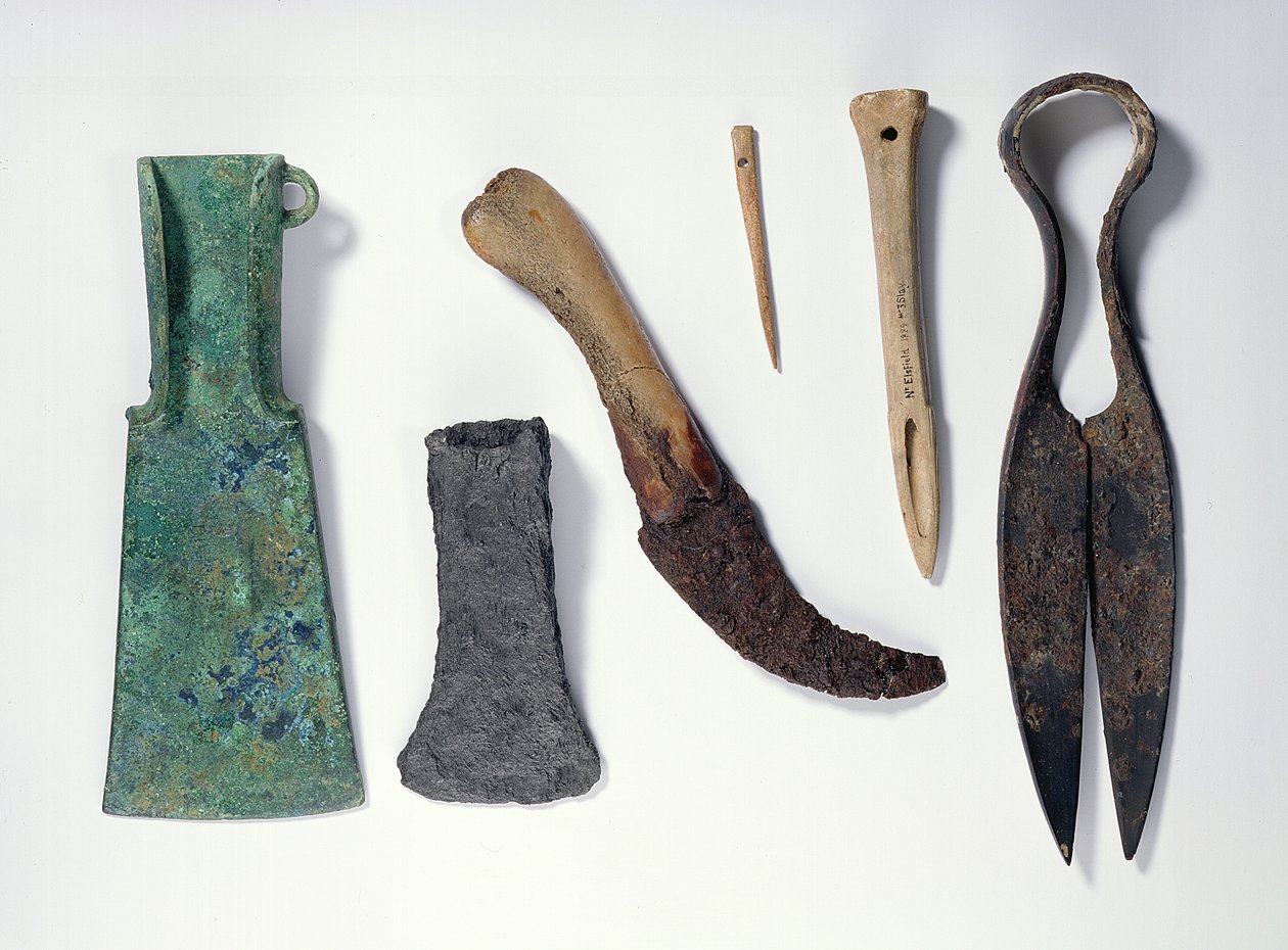 Työkaluvalikoima: L-R: varhaisen rautakauden pronssikirves, jossa taivutetut siivet; myöhemmin rautakirves; veitsi luukahvalla; luun neula; luu awl; rautalevyt tekijältä Iron Age