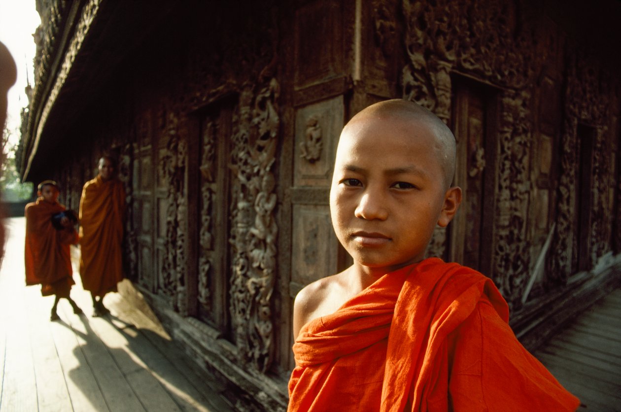 Nuori noviisimunkki veistettyjen teak-paneelien edessä. Shwenandawin luostari, Mandalay, Burma. tekijältä James L Stanfield