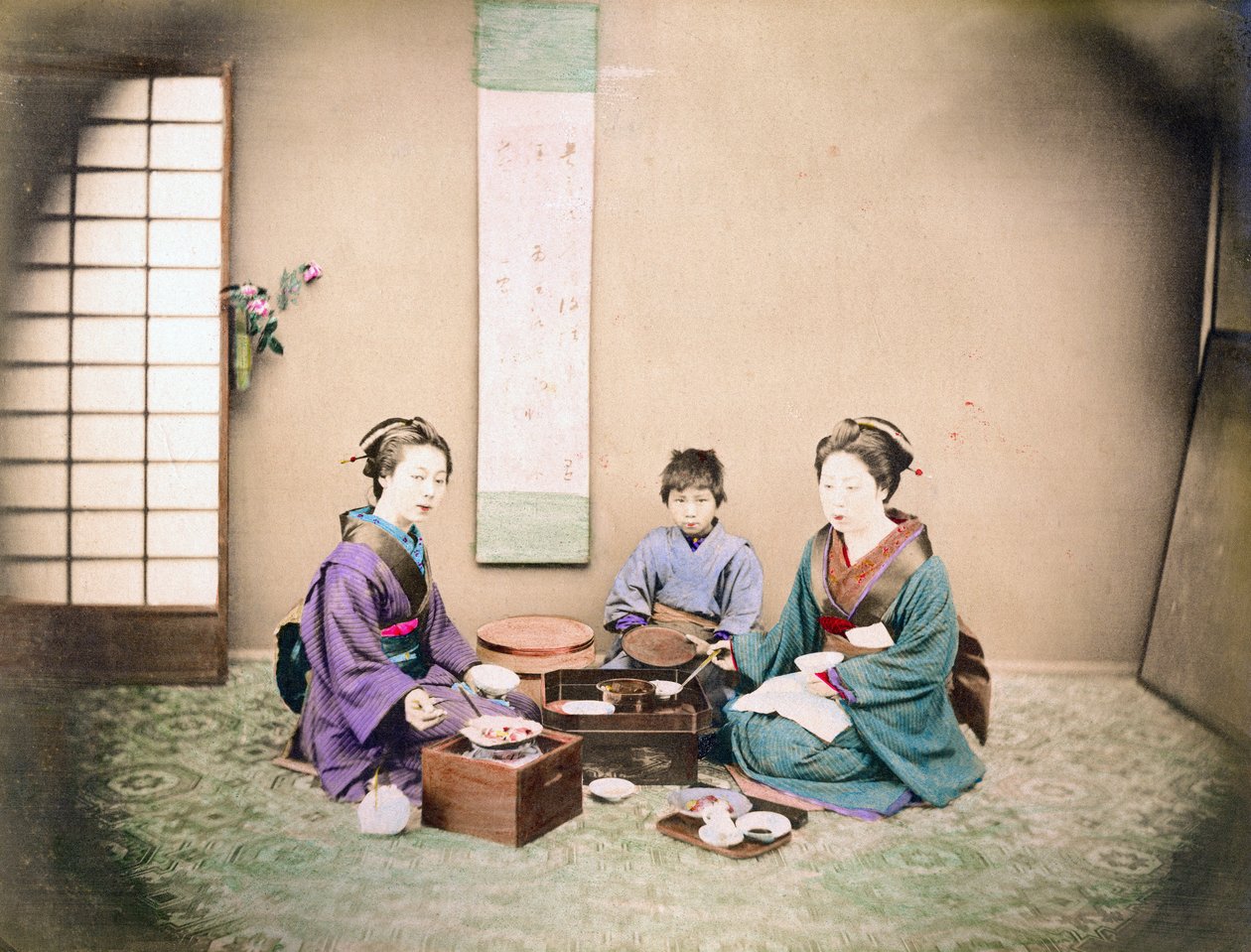 Kaksi naista ja lapsi lounaalla matolla istuen, n. 1890 (käsin väritetty kuva) tekijältä Japanese Photographer