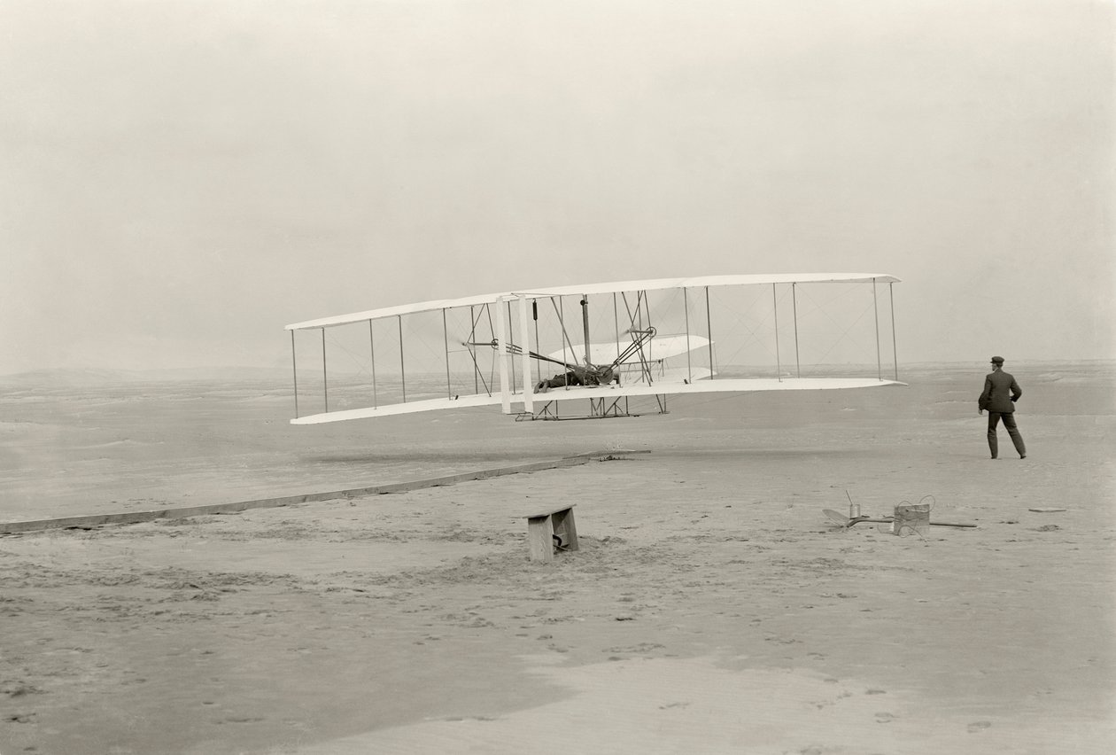 Wright Flyer I tekee ensimmäisen 120 jalan lentonsa 12 sekunnissa Kitty Hawkissa, Pohjois-Carolinassa tekijältä John T. Daniels