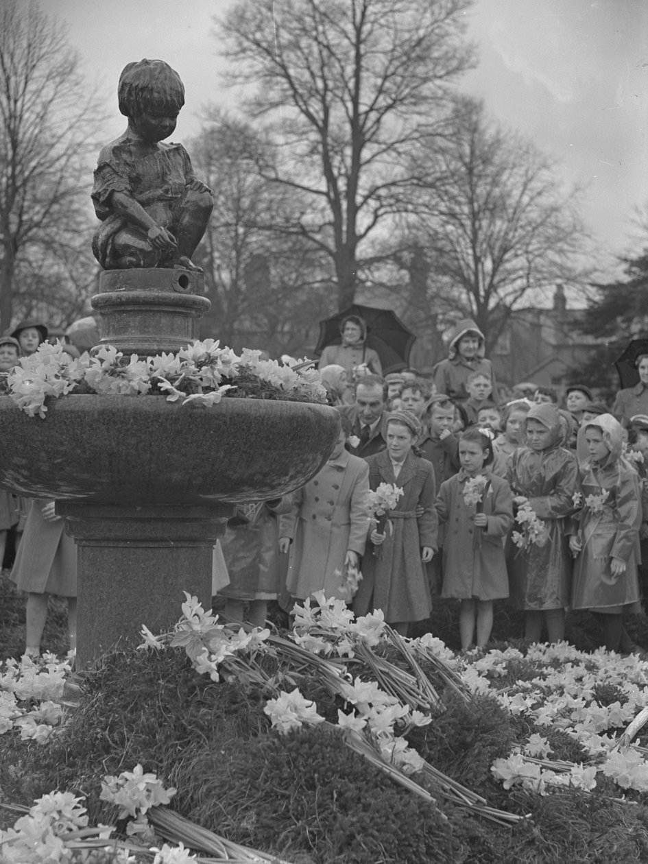 Lapset asettamassa narsissikimppuja suihkulähteelle, jonka päällä on patsas. tekijältä Joseph Hardman