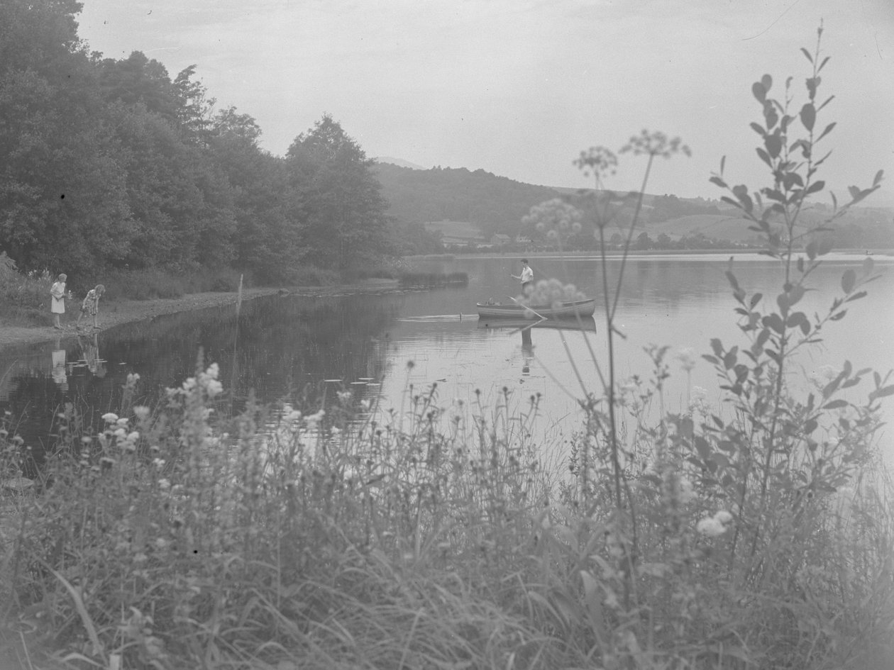 Mies kalastaa veneellä Estwaite Waterillä ja kaksi tyttöä veden äärellä. tekijältä Joseph Hardman