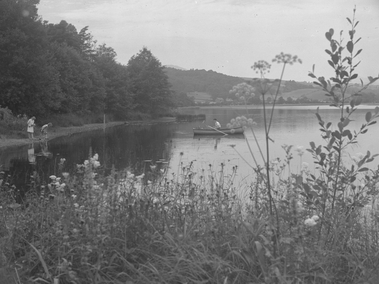 Mies kalastaa veneellä Estwaite Waterillä ja kaksi tyttöä veden äärellä. tekijältä Joseph Hardman