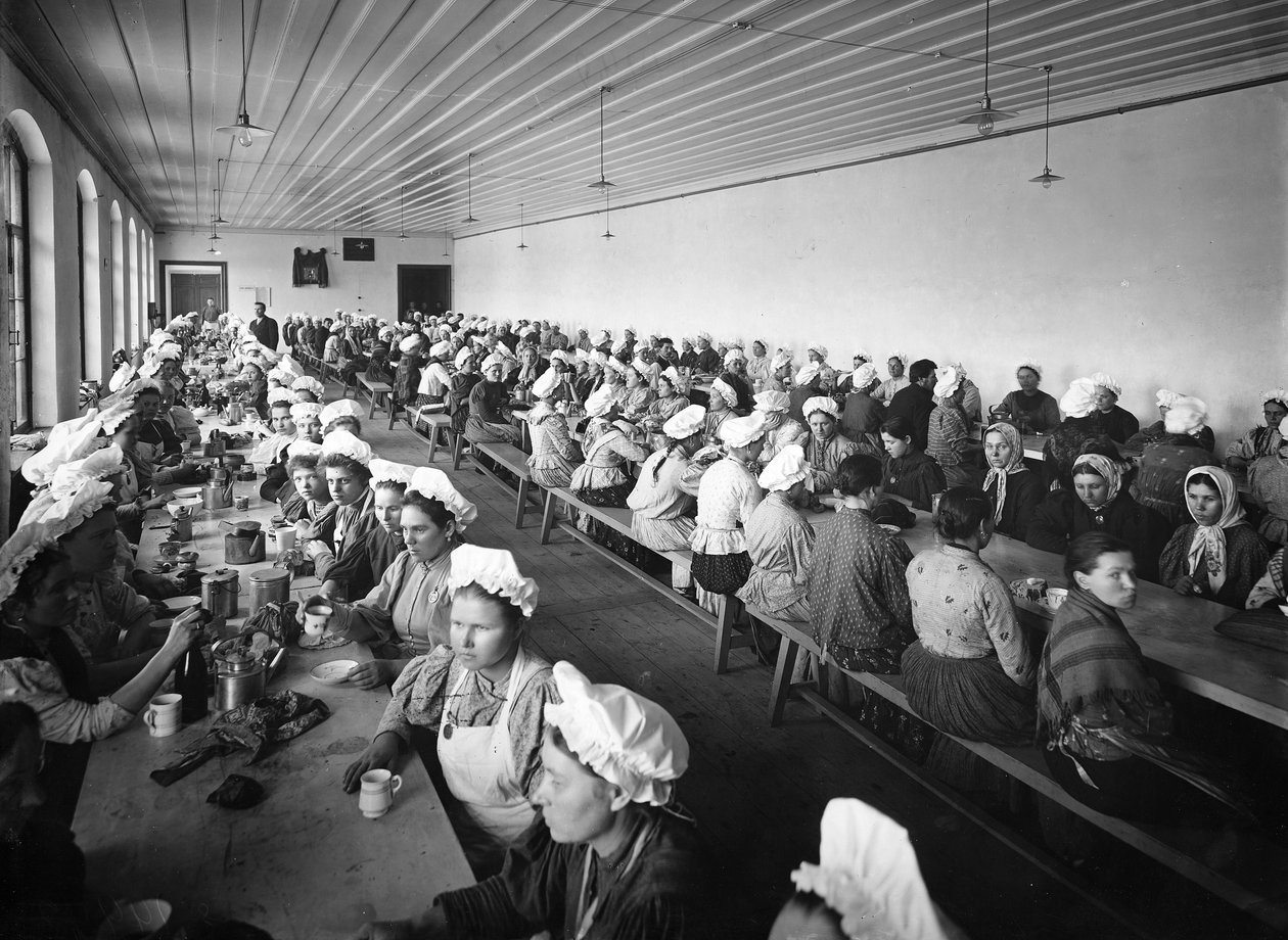 Naistyöntekijät tehtaan varastossa pitävät päivällistauon muutaman miespuolisen valvojan valvonnassa tekijältä Russian Photographer