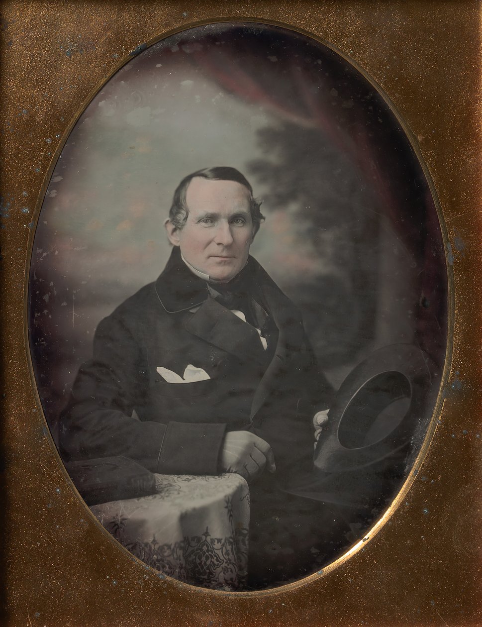 Mies, jolla on takki ja hanskat, pitelee hattua, istuu maalatun ulkotaustan edessä, 1840-luku. tekijältä Samuel Broadbent Jr..