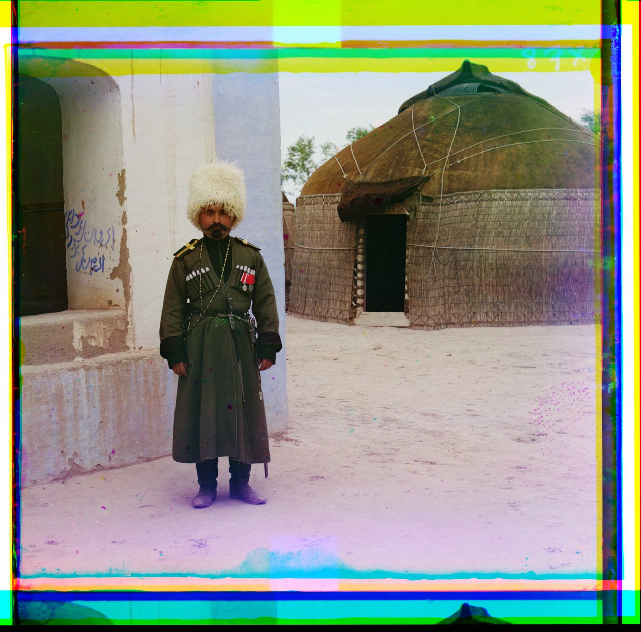 Aseistettu mies univormussa seisoo rakennuksen vieressä, taustalla jurtta, Venäjä, 1915. tekijältä Sergey Prokudin Gorsky