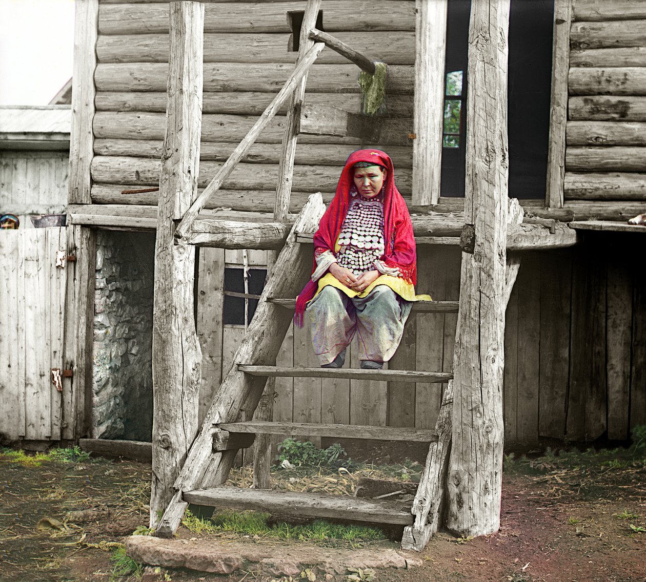 Baškiirinainen kansanpuvussa istumassa puutalonsa portailla, Uralvuoret, Venäjän valtakunta, 1910 tekijältä Sergey Prokudin Gorsky