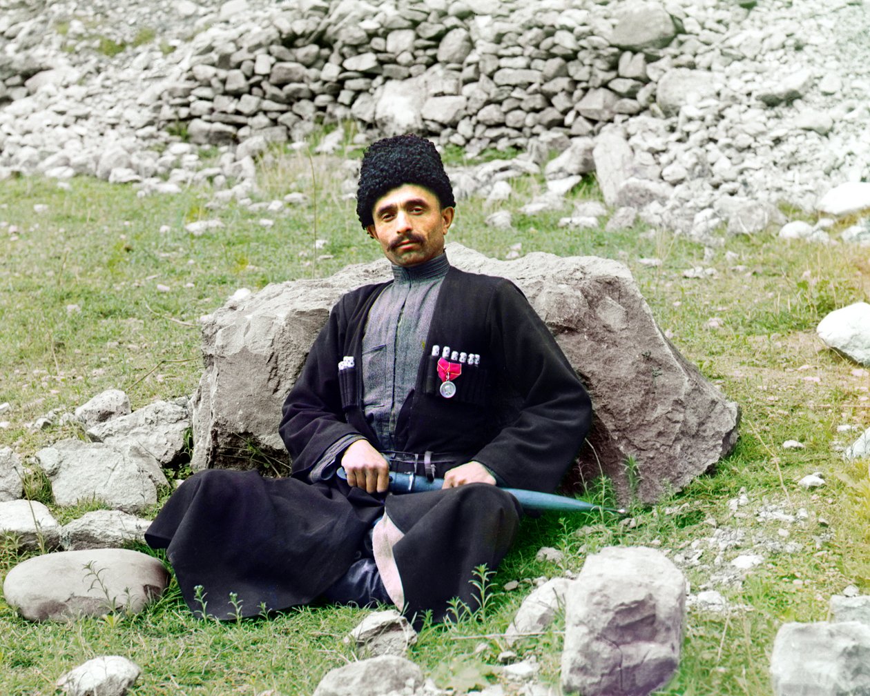Dagestanin tyypit - Sunnimuslimimies, jolla on yllään perinteinen mekko ja päähineet, tupattu tikari kyljellään istuu maassa, Venäjän valtakunta, vuosina 1905-1915 tekijältä Sergey Prokudin Gorsky