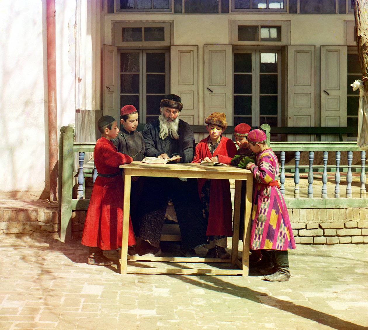 Ryhmä juutalaisia lapsia opettajan kanssa pöydällä talon edessä, Samarkand, Venäjän valtakunta, vuosina 1905-1915 tekijältä Sergey Prokudin Gorsky