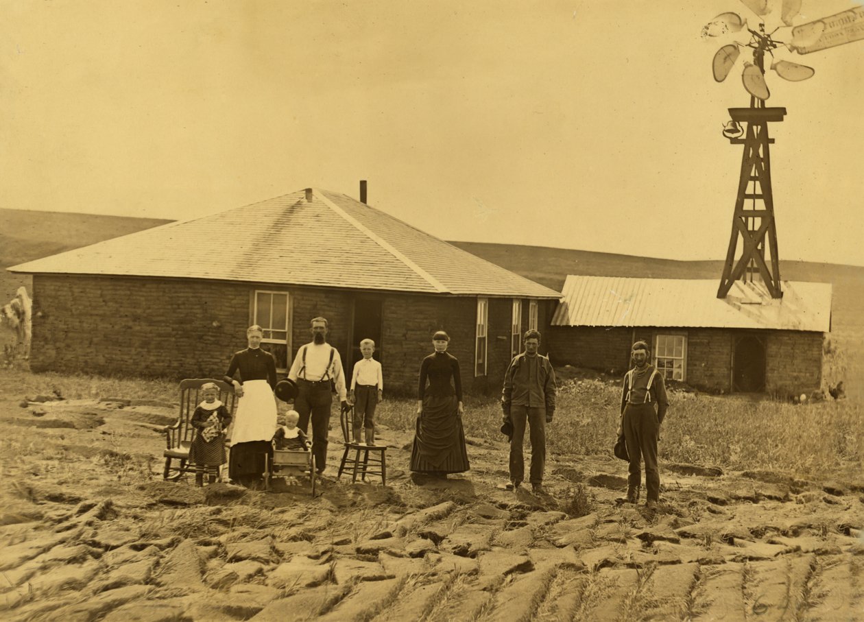 Kotitalousperhe, heidän turvetalonsa ulkopuolella, jossa on tuulimylly viereisen rakennuksen katolla Custerin piirikunnassa, Nebraskassa, n. 1885 (b/w kuva) tekijältä Solomon D. Butcher