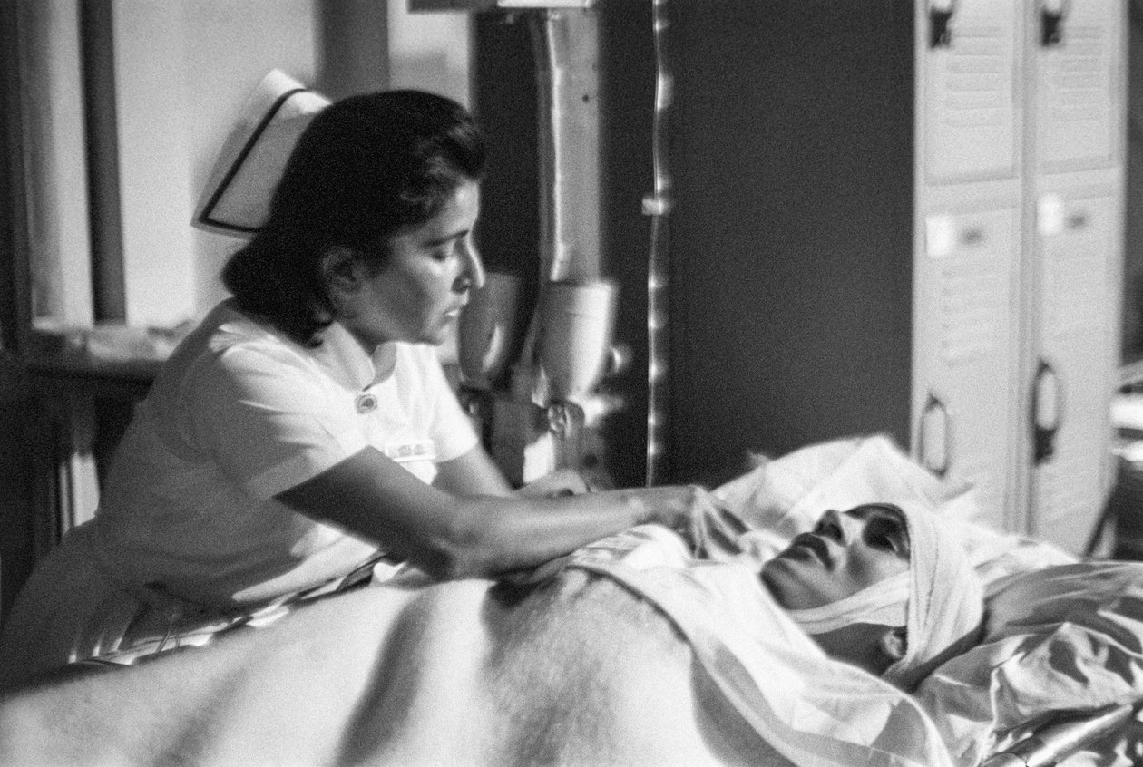 Sairaanhoitaja auttaa potilasta venytettynä leikkauksen jälkeen sairaalalaiva SS Hopella. tekijältä Ted Spiegel