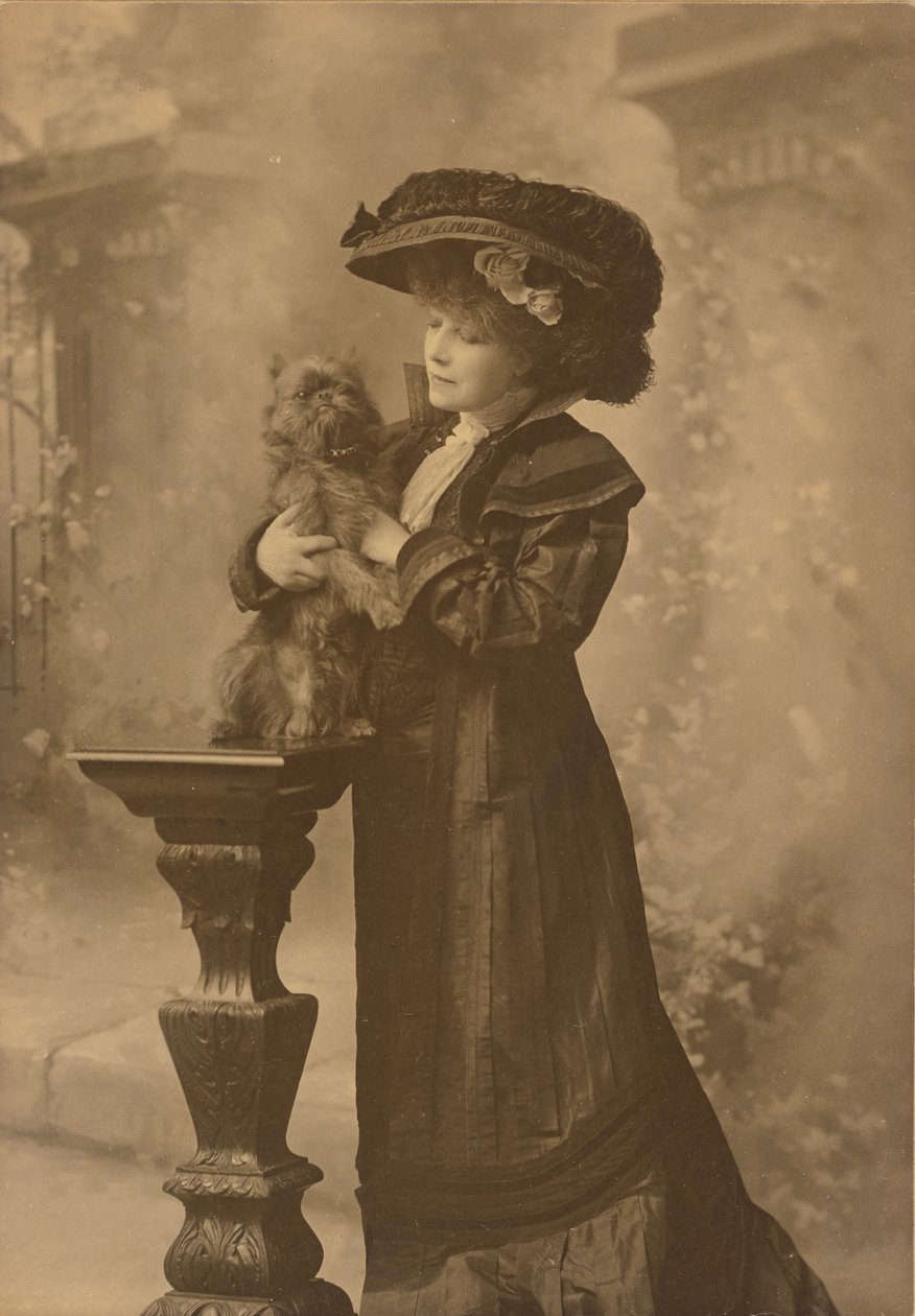[Sarah Bernhardt seisoo ateljeeympäristössä ja pitää pientä mustaa koiraa koristeellisella, veistetyllä puujalustalla] tekijältä Theodore C. Marceau