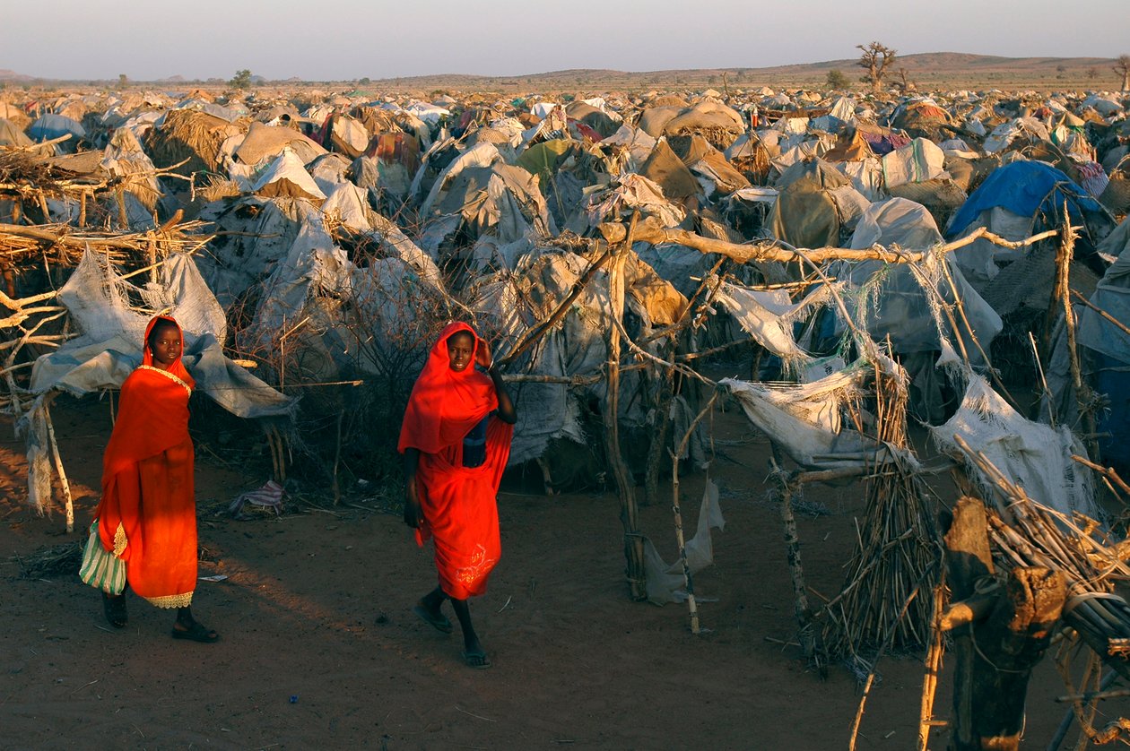 Kirkkaan punaisiin vaatteisiin pukeutuneena naiset kävelevät Otashin sisäisten pakolaisten leirin läpi tekijältä Unbekannt Unbekannt