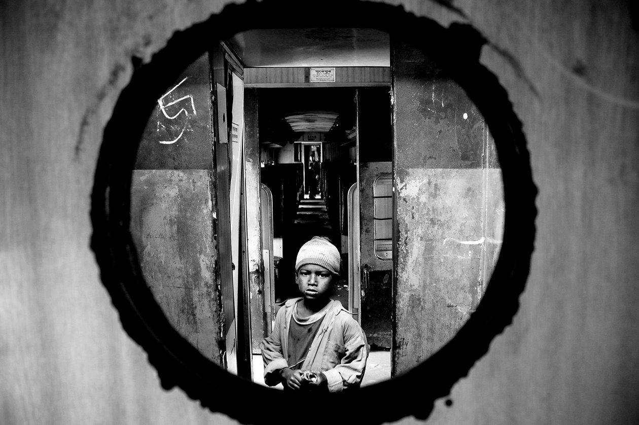 Muotokuva katulapsesta nähtynä junan osaston oven reiästä Kamalapurin rautatieasemalla Dhakassa, Bangladeshissa. 5. tammikuuta 2007. tekijältä Unbekannt Unbekannt